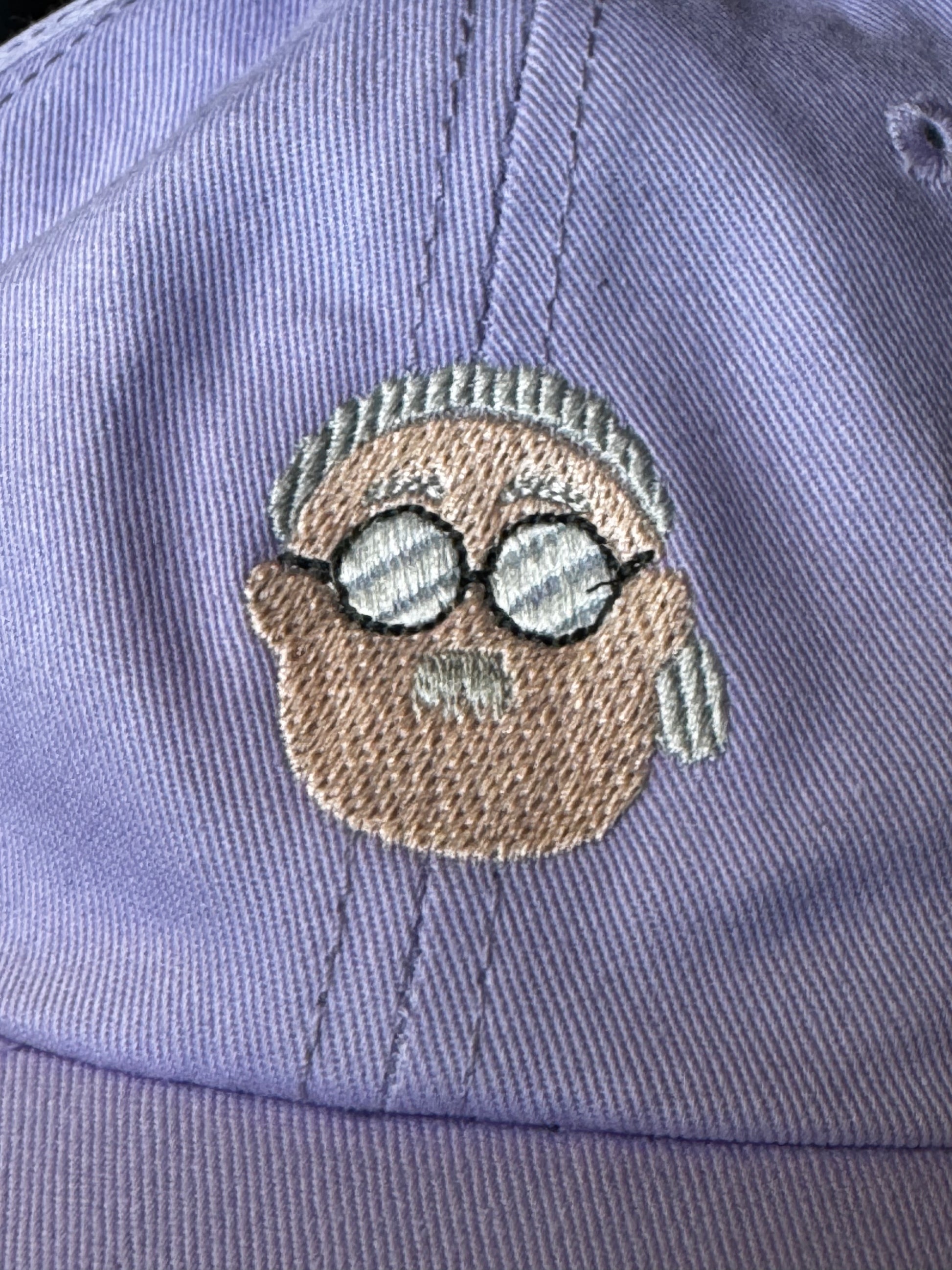 Purple cap with embroidered face design wearing glasses on a matching background